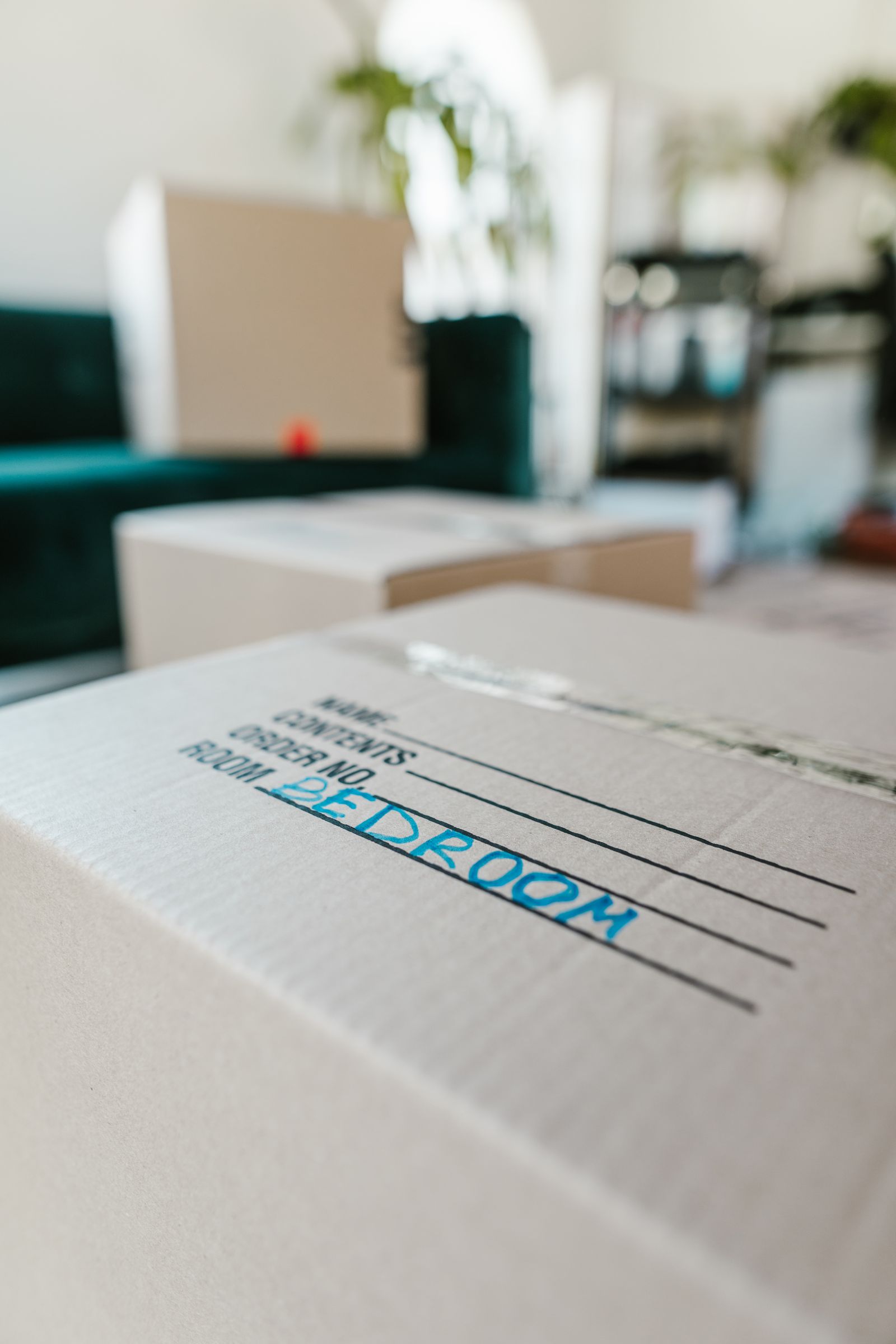A hand writing the room name on a labelled moving box beside a tape dispenser