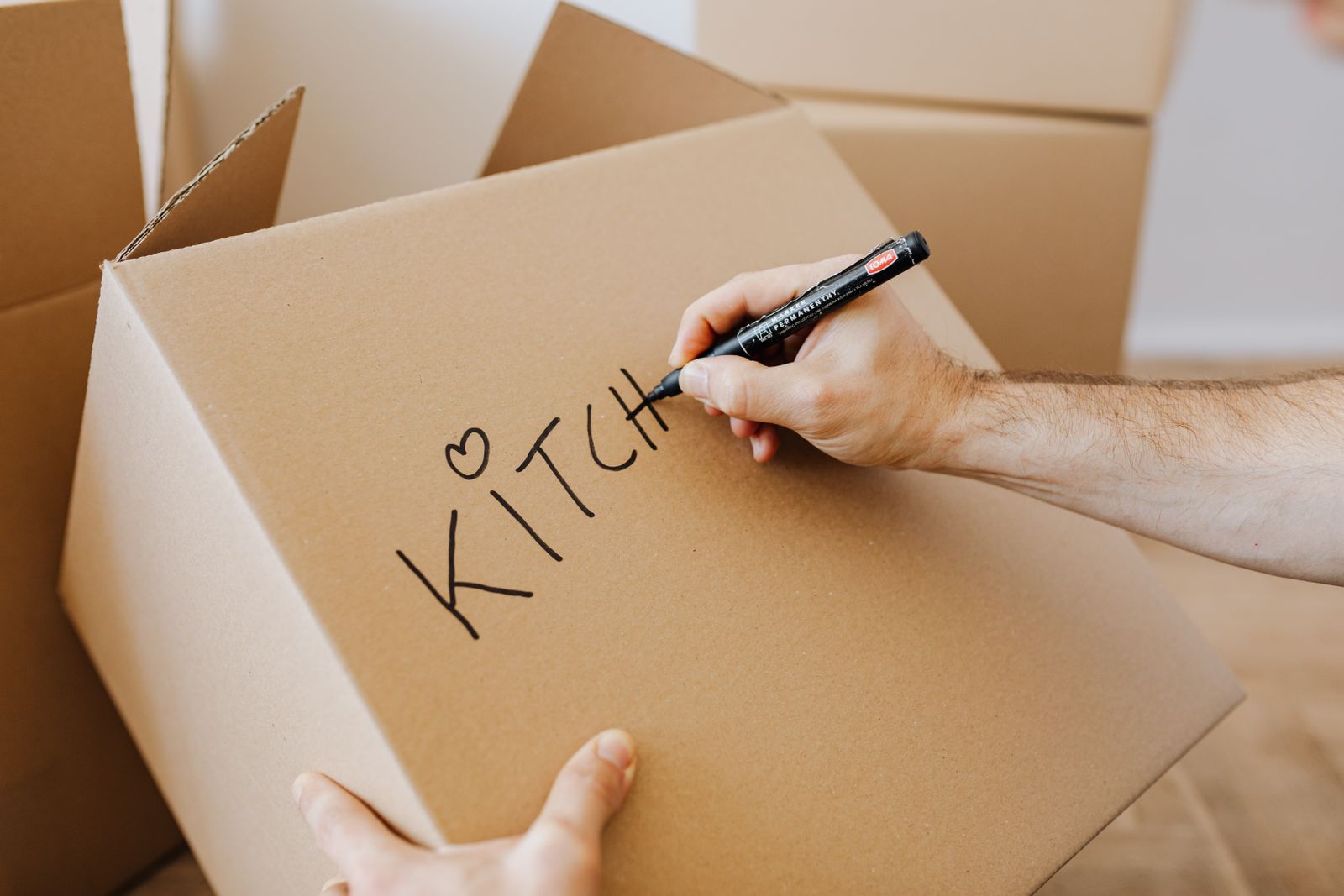 Hands labelling packed cardboard moving boxes with a marker, seen from above